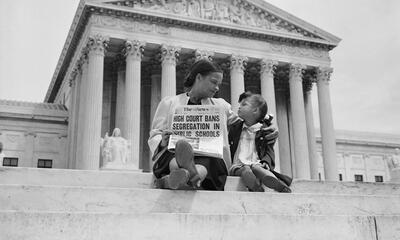 Image of woman and child on the steps of the Supreme Court with a newspaper with headline about the Brown decision